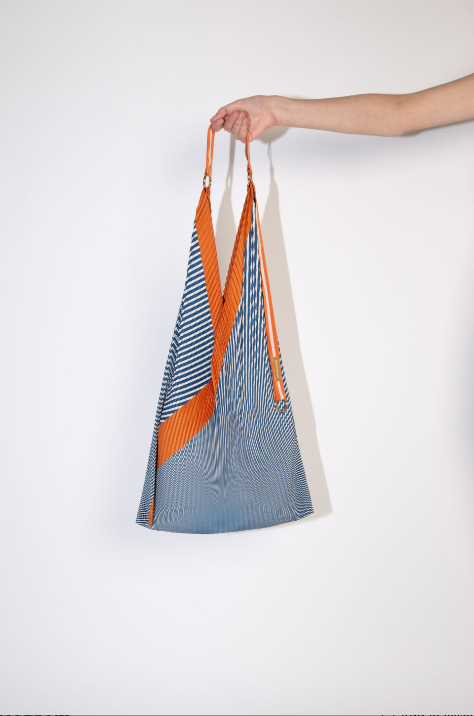 Bolso tote plisado modelo Anna Rust en azul y naranja de Multitudes, hecho en poliéster reciclado con asas de satén, diseño sostenible y elegante, fabricado en Italia.