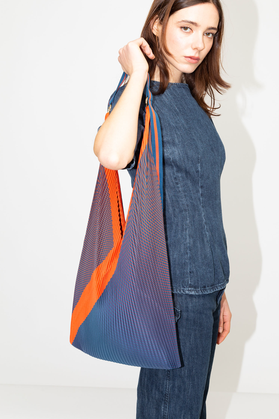 Bolso plisado Isabella Blue de Multitudes en tonos azul y naranja, con asas de satén resistentes y anilla dorada para colgar accesorios. Diseño elegante y sostenible en poliéster reciclado.