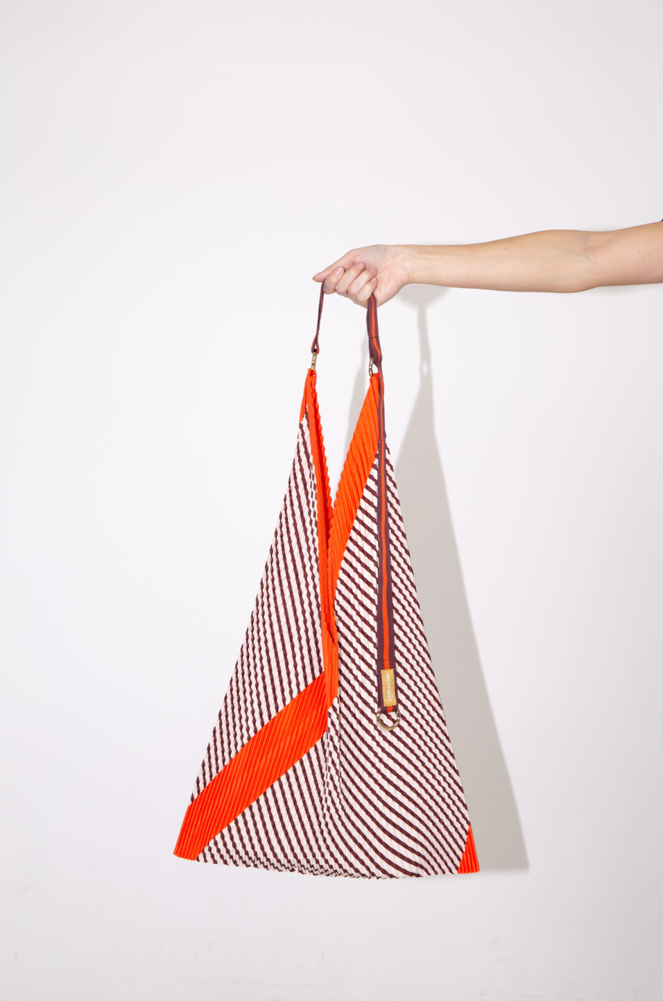 Bolso tote plisado Francesca Red de Multitudes en tonos burdeos y naranja, confeccionado en poliéster reciclado con acabado satinado efecto seda, con asas de satén resistentes y anilla dorada para accesorios. Ideal para uso diario con estilo y sostenibilidad.