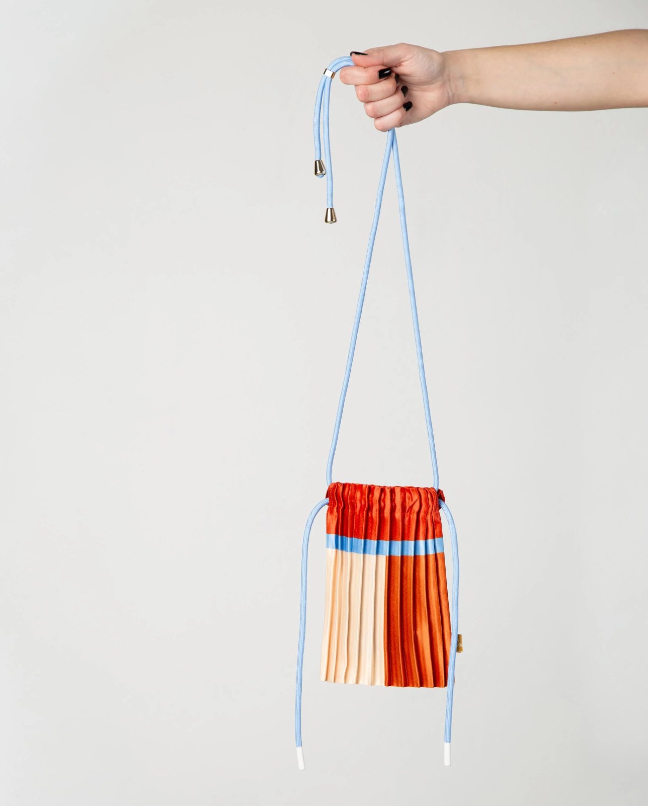 Multitudes pleated mini bag Siena terracotta blue held by hand side view