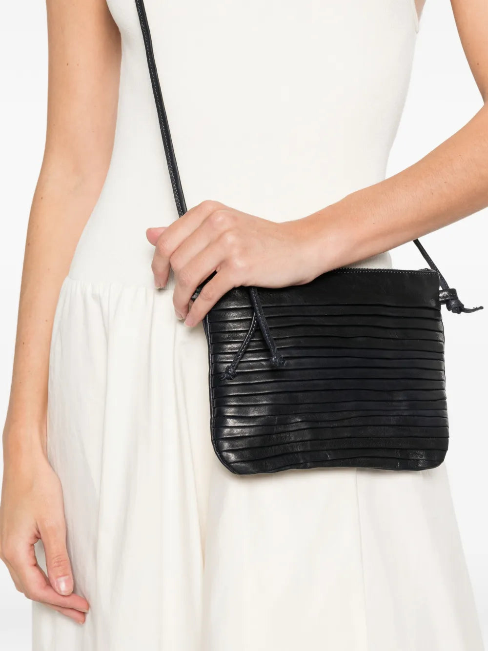 Small navy blue leather crossbody bag with horizontal pleated texture and adjustable strap, handcrafted in Italy, displayed on a white background.