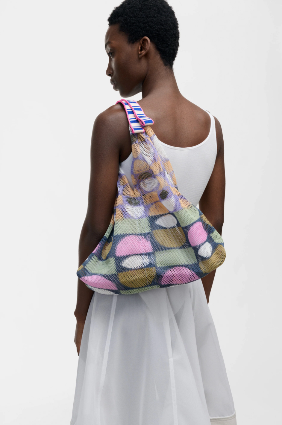 Small Udaipur Sage multicolor patchwork mesh tote bag with blue and pink striped handles, worn on the shoulder by a model