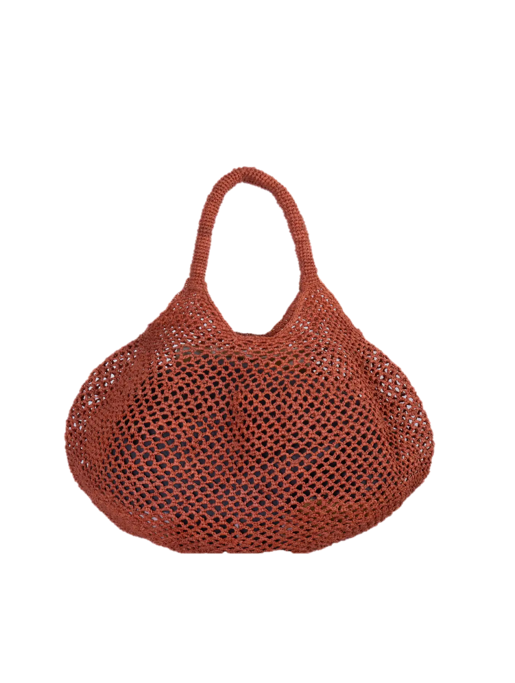 Cesta calada de rafia natural color teja de Sans-Arcident, bolso artesanal hecho a mano en Madagascar, ideal como bolso de verano o complemento sostenible para looks casuales.