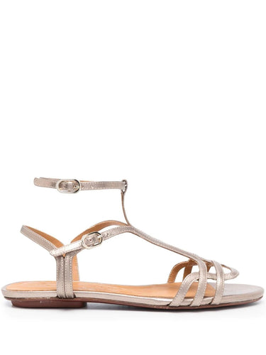 Sandalia plana Chie Mihara YAEL en piel plateada con cierre doble al tobillo, hebilla lateral y puntera abierta. Suela plana de cuero y goma, diseño cómodo y elegante.