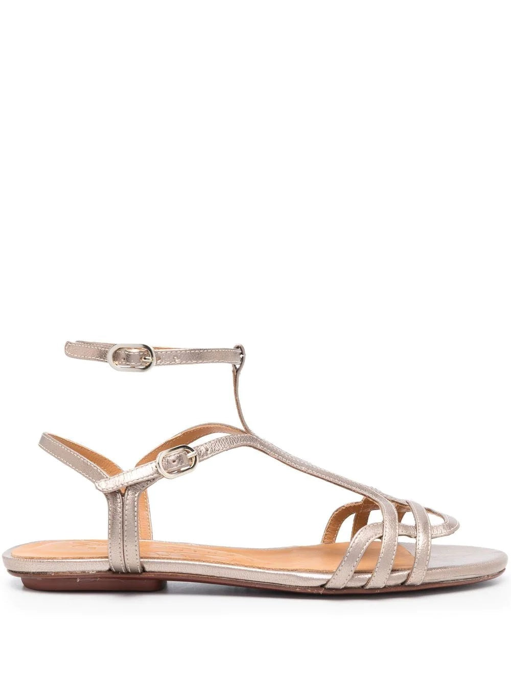 Sandalia plana Chie Mihara YAEL en piel plateada con cierre doble al tobillo, hebilla lateral y puntera abierta. Suela plana de cuero y goma, diseño cómodo y elegante.