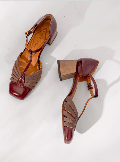 Par de zapatos modelo Vudui con tacón medio, acabado en charol burdeos y tiras en T; diseño retro, elegante y atemporal — Pair of Vudui medium-heel shoes in burgundy patent leather with T-strap detail, retro, elegant and timeless design.