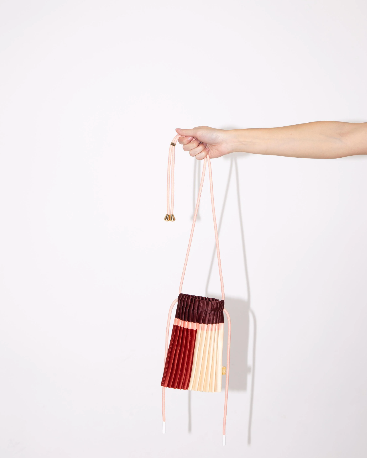 Multitudes pleated mini bag Rubi burgundy red pink cream held by hand side view
