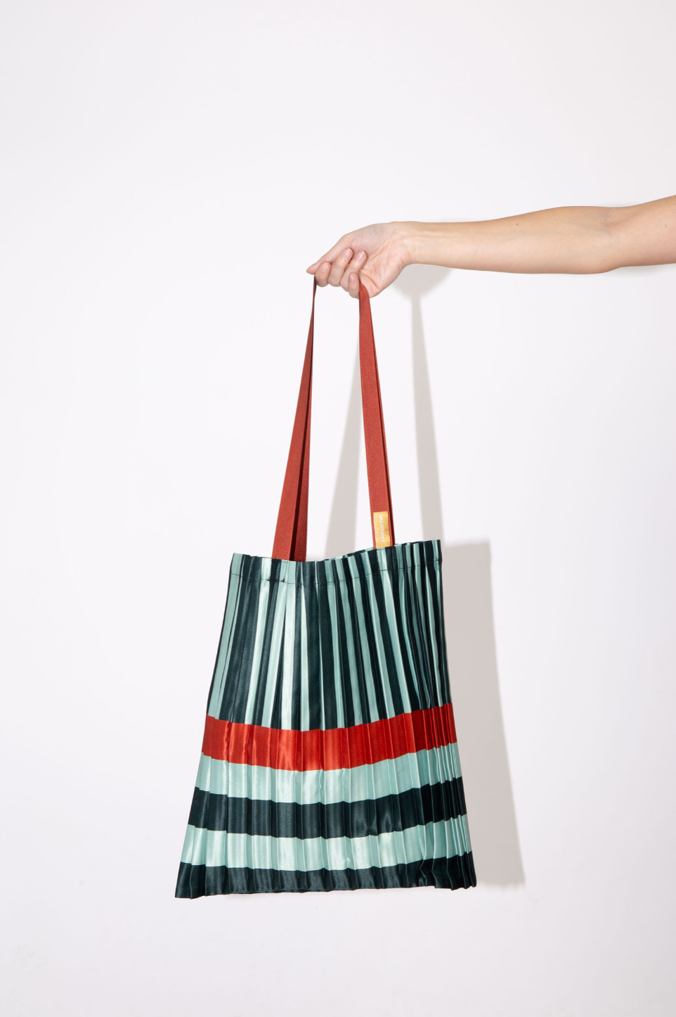 Bolso tote Smeralda plisado de Multitudes en verde y naranja. Diseño elegante y sostenible fabricado en Italia con satén reciclado.

