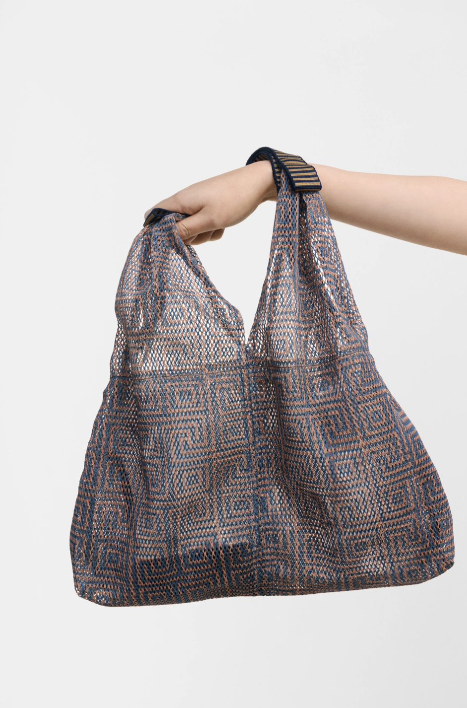Small Udaipur Rosso dark grey geometric woven mesh tote bag with black and gold striped handles, held by hand
