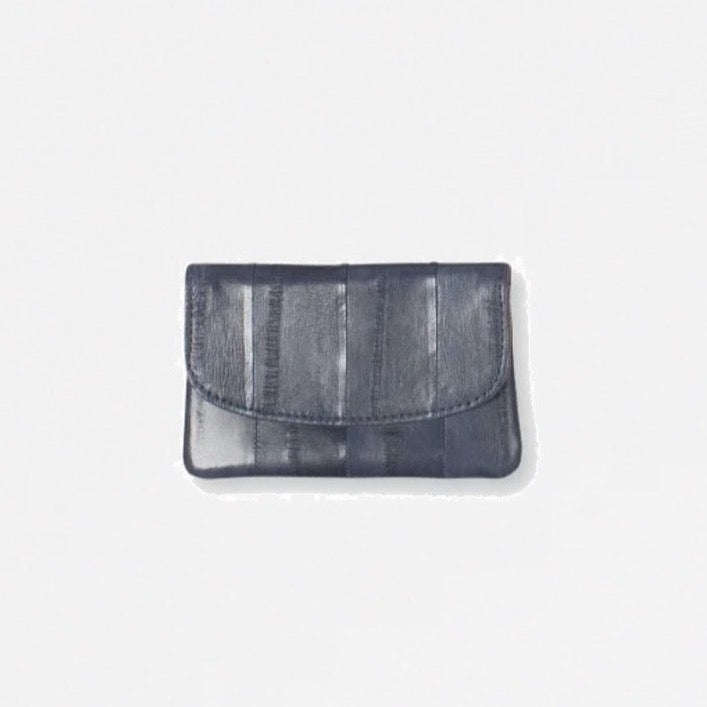 Monedero gris con solapa y cierre a presión, en piel de anguila suave, compartimentos para tarjetas de crédito.   Medidas: Ancho: 11 cm, altura: 7 cm.  Forro interior 100 % algodón.  Material exterior: 100% piel de anguila.   